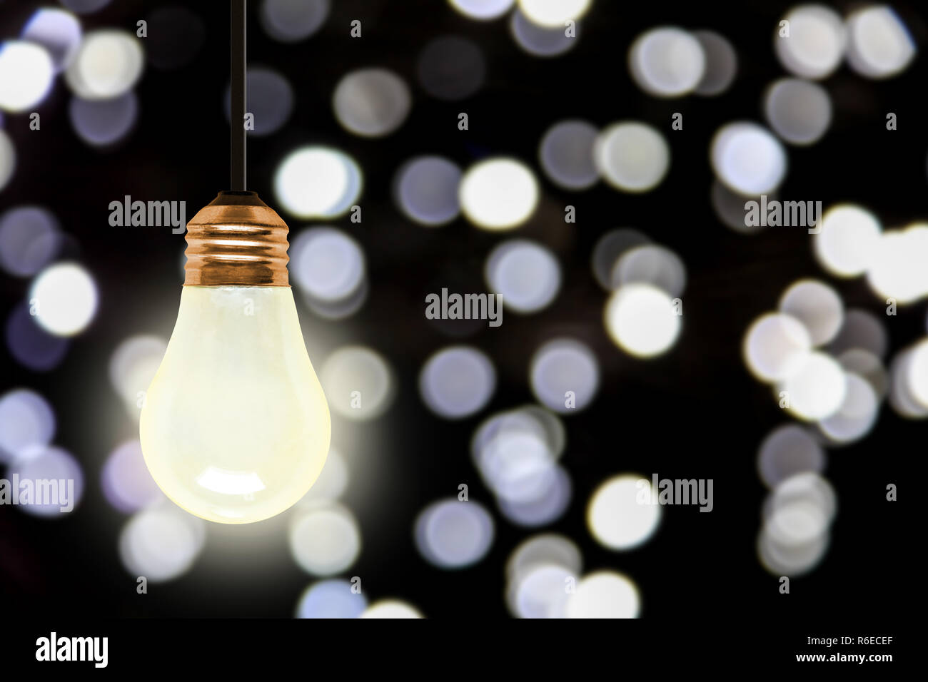 Illuminating light bulb hanging with colorful blurred Christmas lights bokeh effect and copy space. Stock Photo