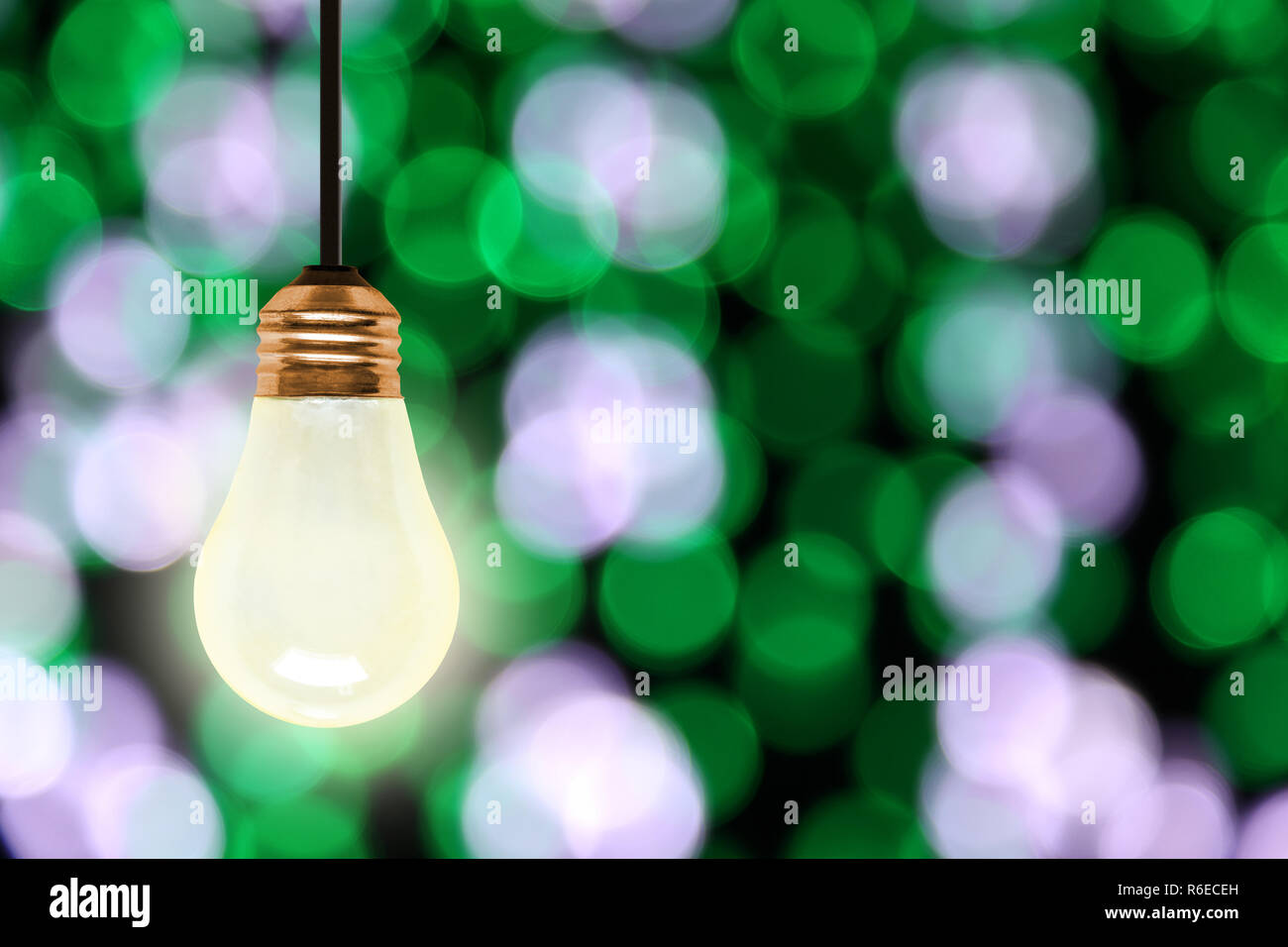 Illuminating light bulb hanging with colorful blurred Christmas lights bokeh effect and copy space. Stock Photo