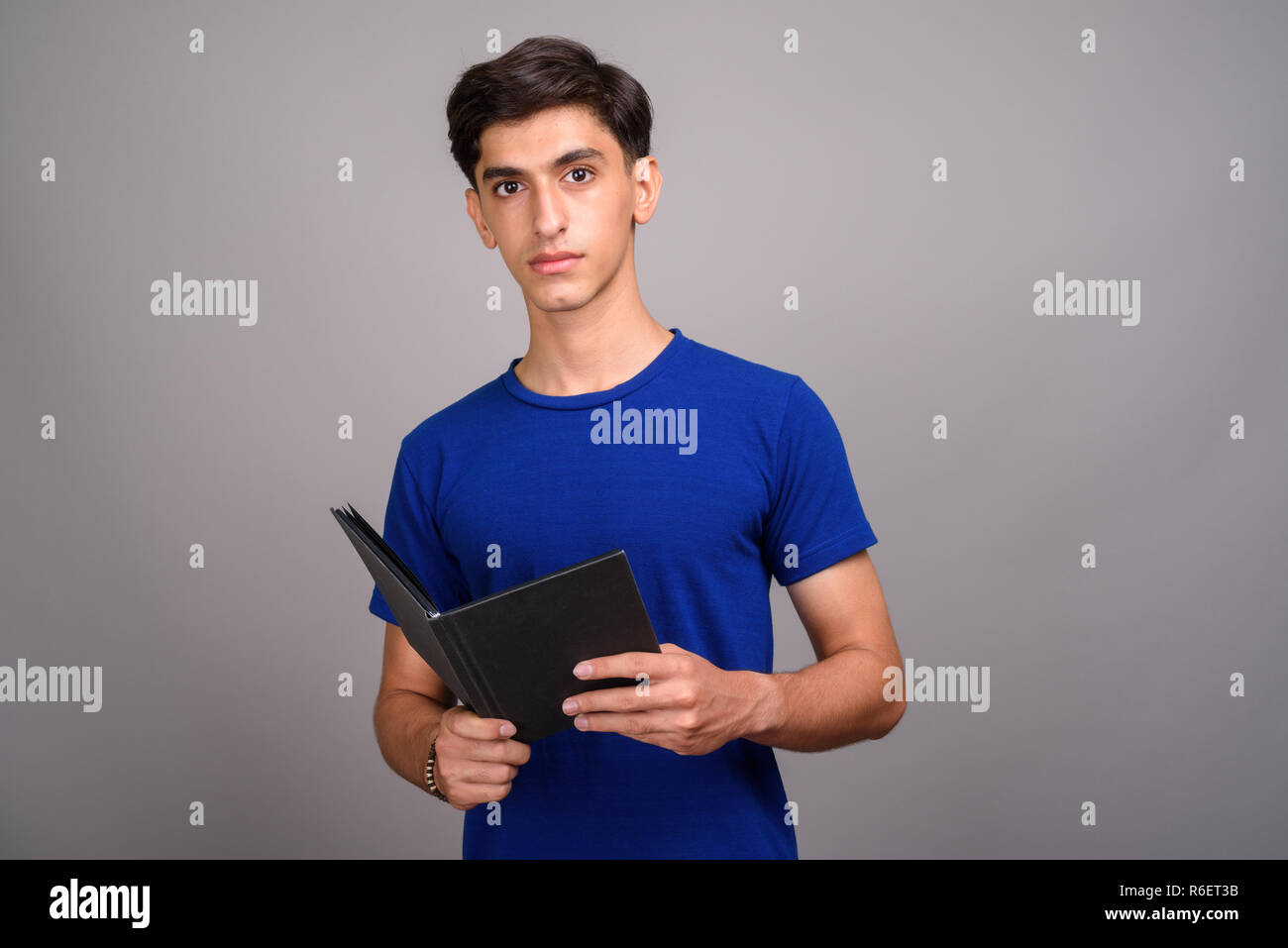 Young handsome Persian teenage boy student holding book Stock Photo