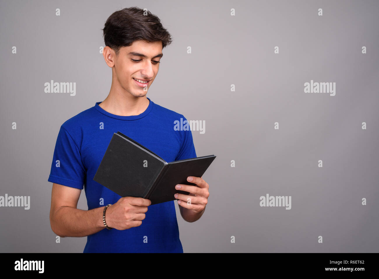Young handsome Persian teenage boy student holding book Stock Photo