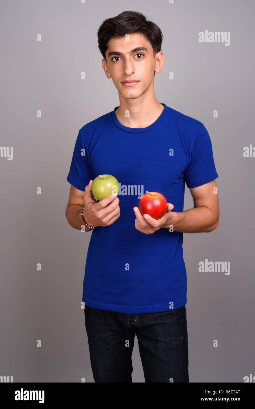 Young handsome Persian teenage boy holding healthy green and red apple ...