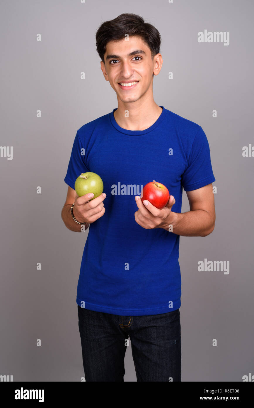 Young handsome Persian teenage boy holding healthy green and red apple ...
