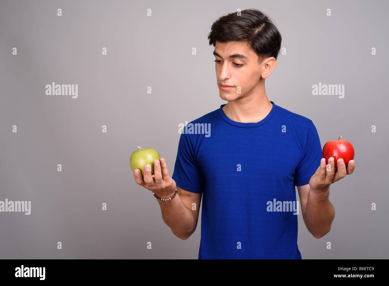 Young handsome Persian teenage boy holding healthy green and red apple ...