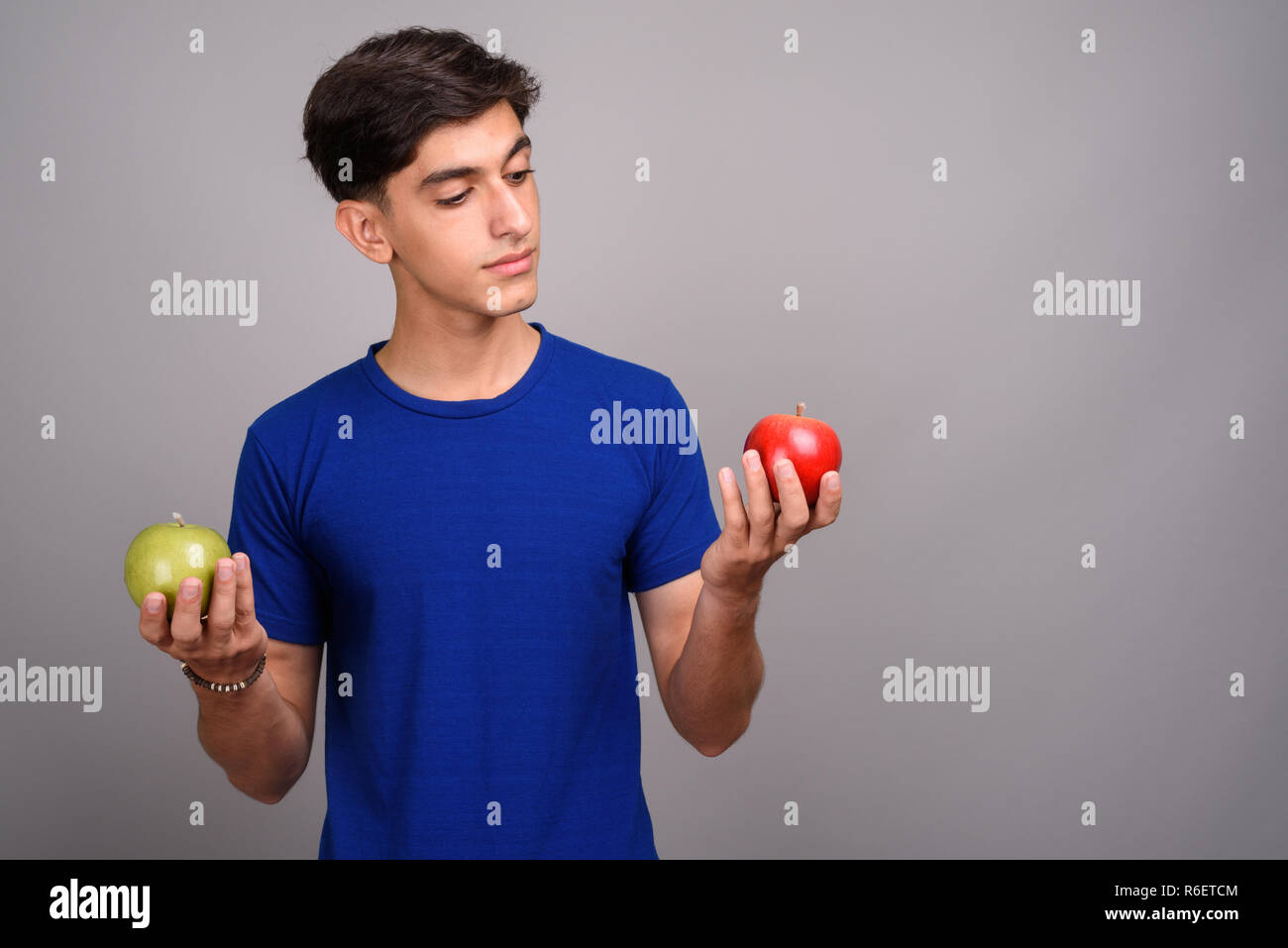 Young handsome Persian teenage boy holding healthy green and red apple ...