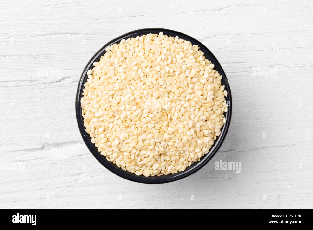 Sesame seeds in iron cast mug on white wooden background, view directly from above Stock Photo