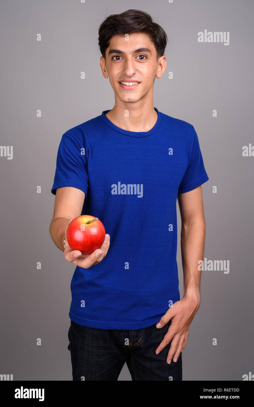Young handsome Persian teenage boy holding healthy apple Stock Photo