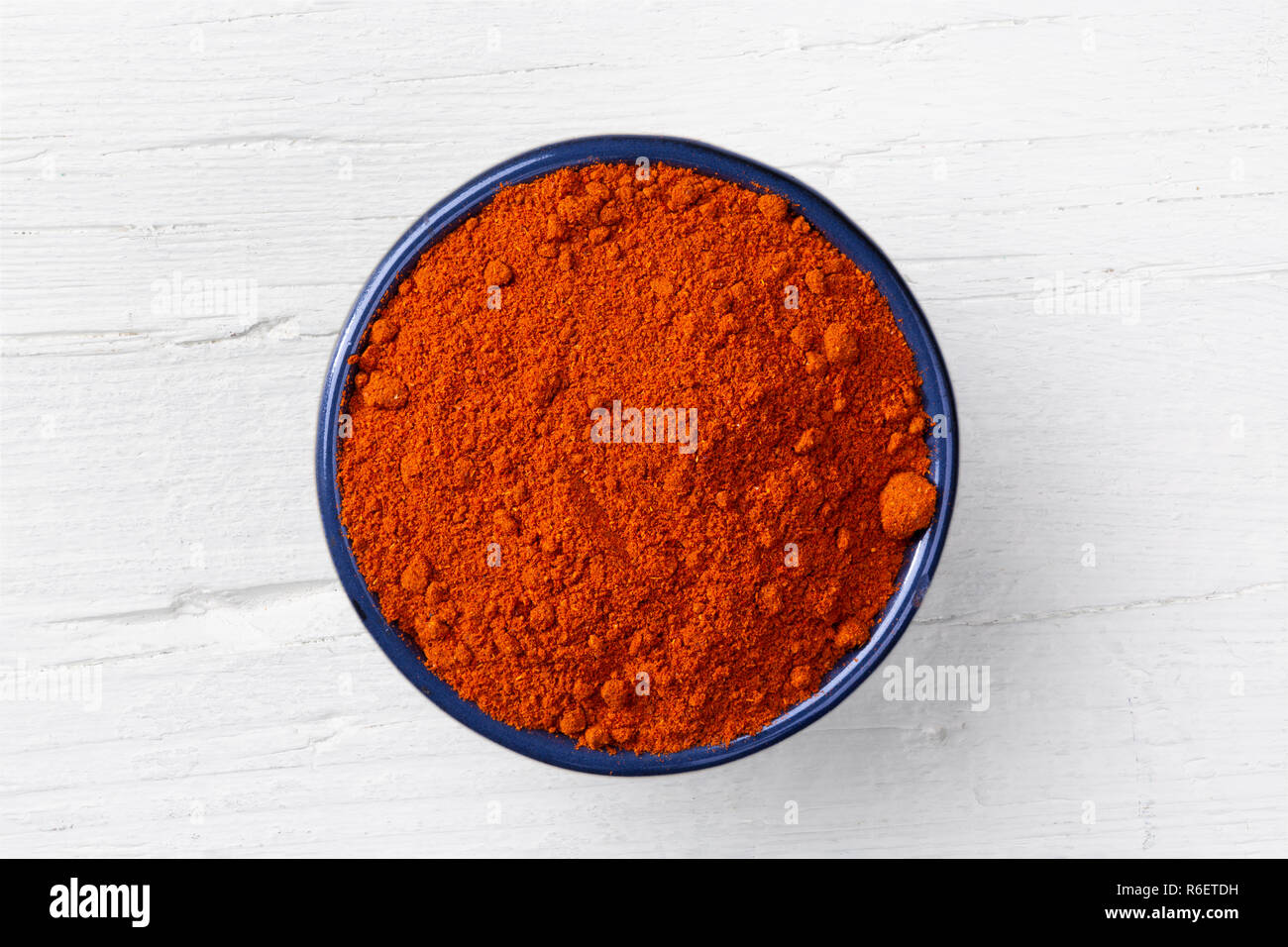 Chili paprika powder in cast iron bowl on white wooden background, view