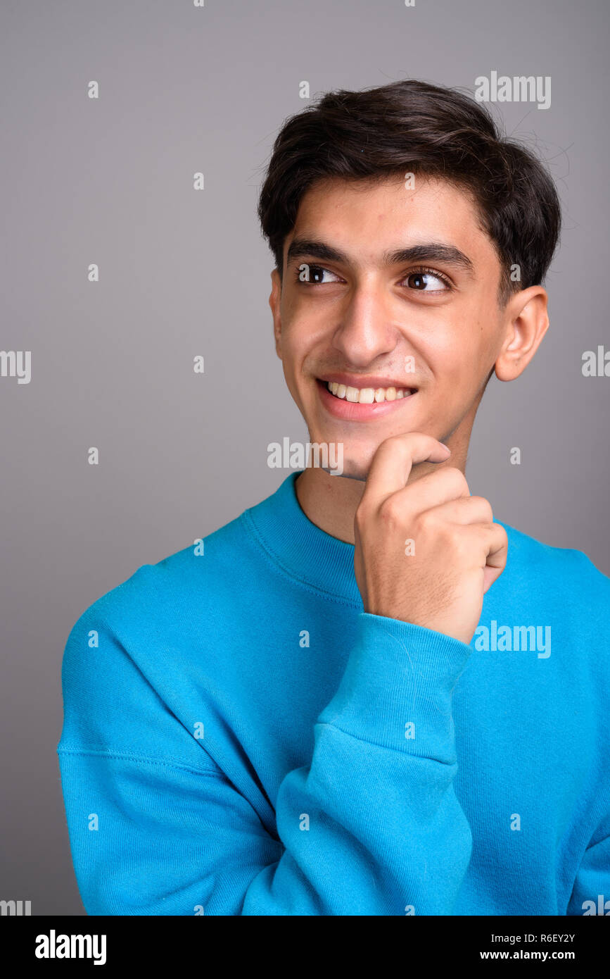 Young happy Persian teenage boy smiling and thinking Stock Photo