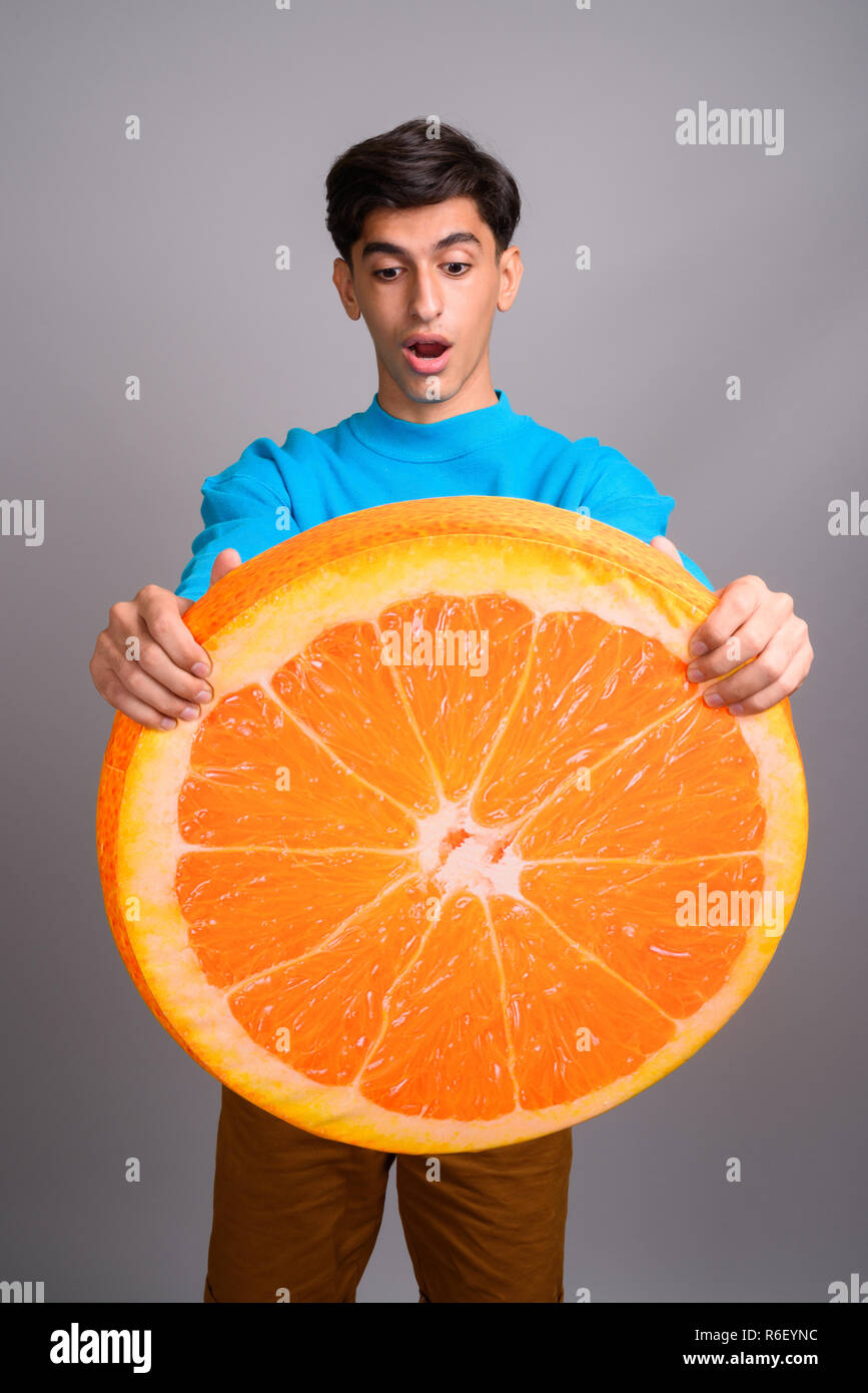Young Persian teenage boy holding big slice of orange fruit Stock Photo