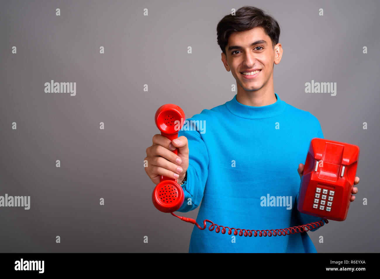 Young handsome Persian teenage boy talking on red old phone Stock Photo