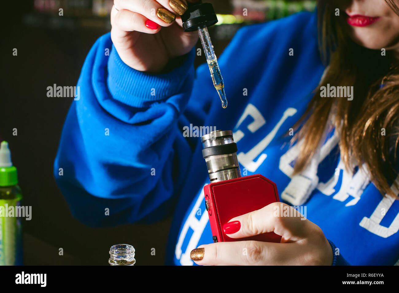 elfbar elfa master akku young Cute woman, the seller in vape shop shop, smoking electronic  cigarette, fills the tank juice Stock Photo