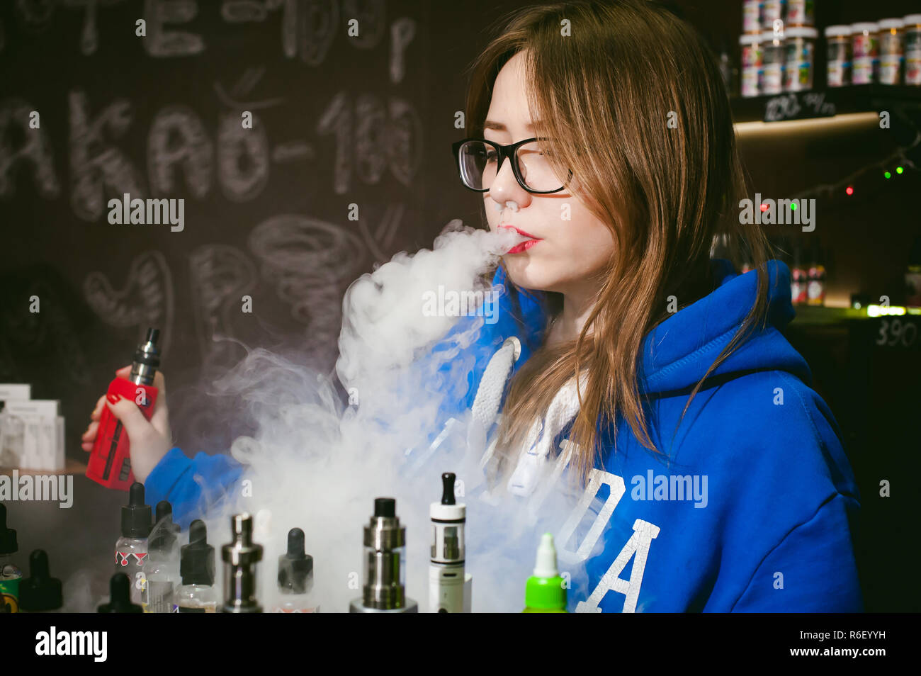 vape verkäufer young Cute woman, the seller in vape shop shop, smoking electronic  cigarette, vaping and releases a cloud of vapor Stock Photo