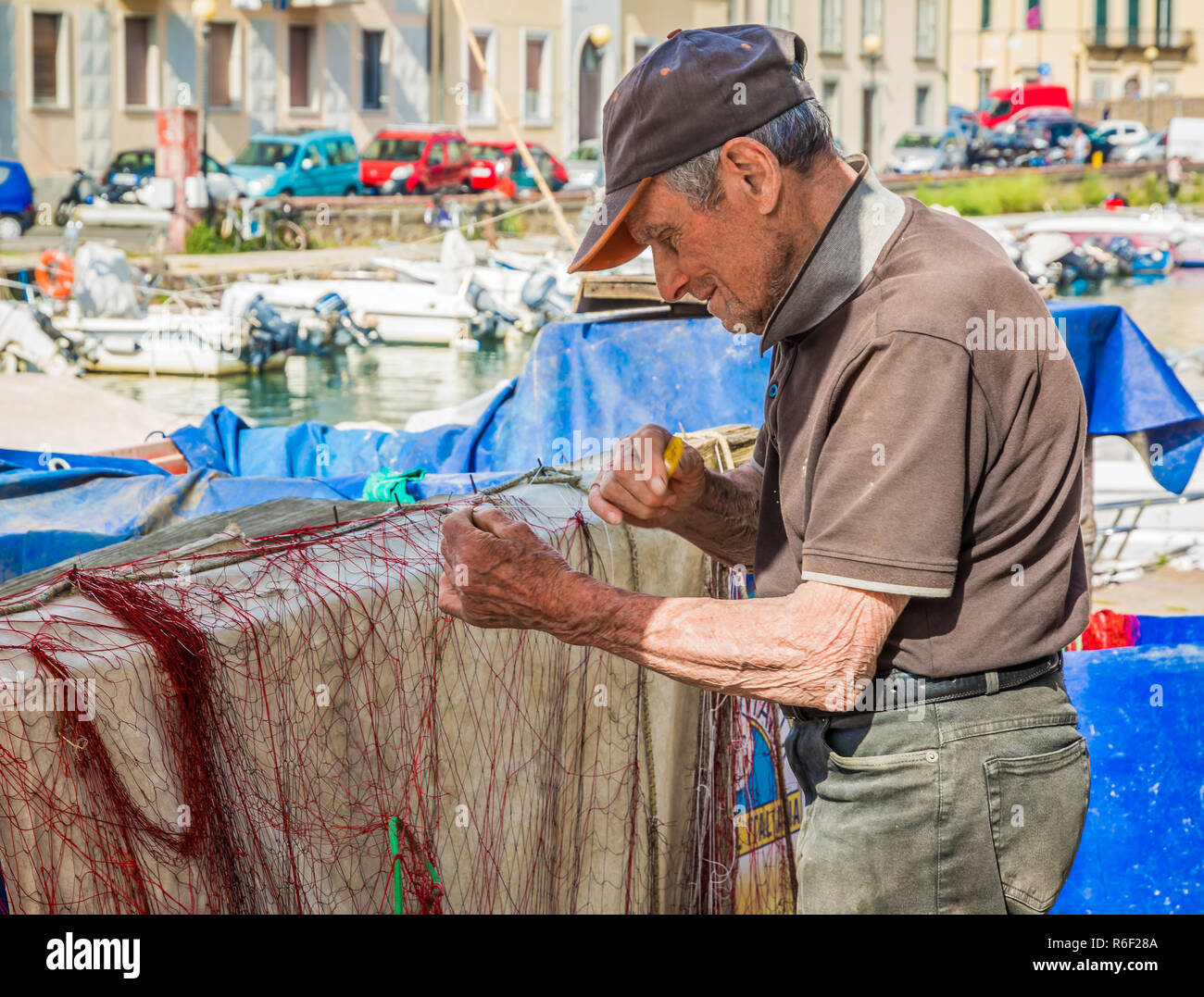 old fisherman repairing the net for fishing on an area that many call Piccola Venezia or little Venice, city of Livorno in Tuscany, Italy Stock Photo