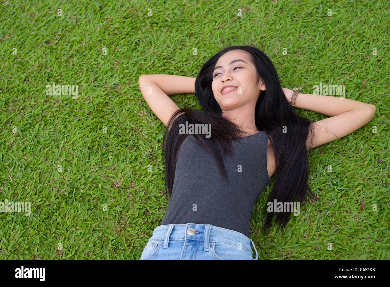 Happy young beautiful Asian woman laying down on grass at the park Stock Photo