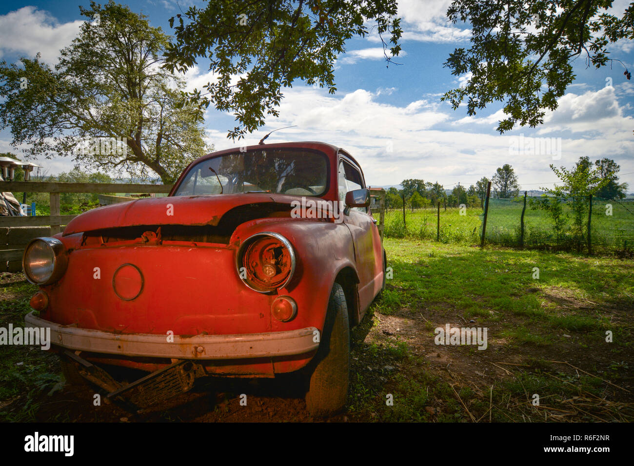 Old abandoned small red car under the tree in the coutryside Stock Photo