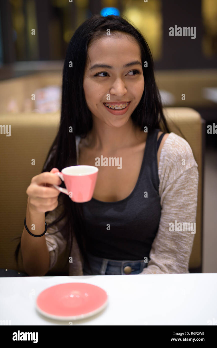 Happy young beautiful Asian woman relaxing inside the coffee shop Stock Photo