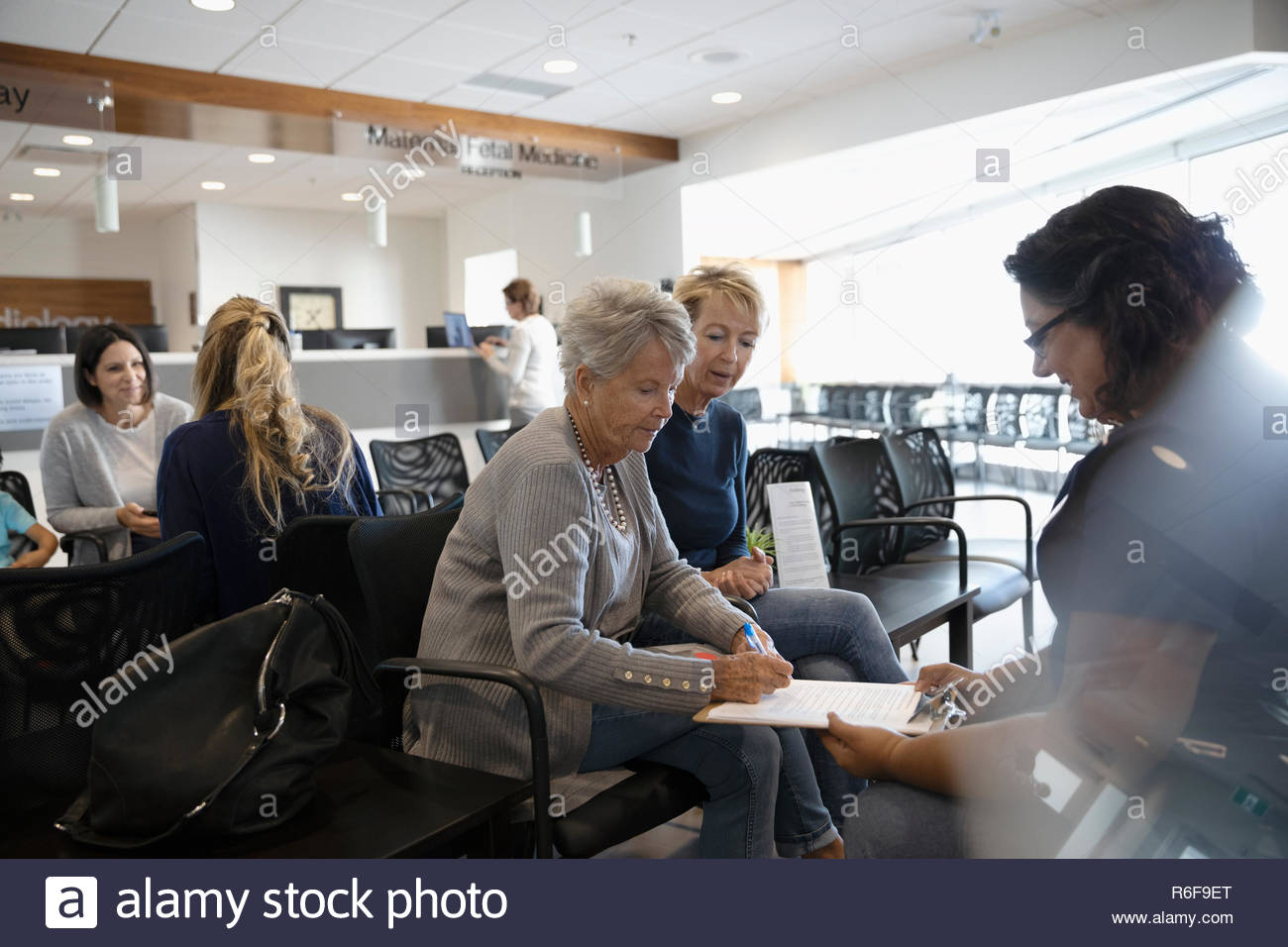 Female nurse discussing insurance paperwork with senior patient in clinic waiting room Stock Photo