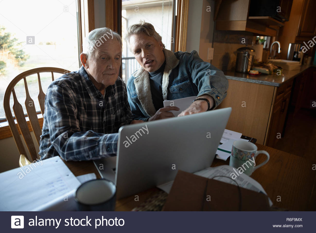 Male farmers paying bills at laptop in kitchen Stock Photo