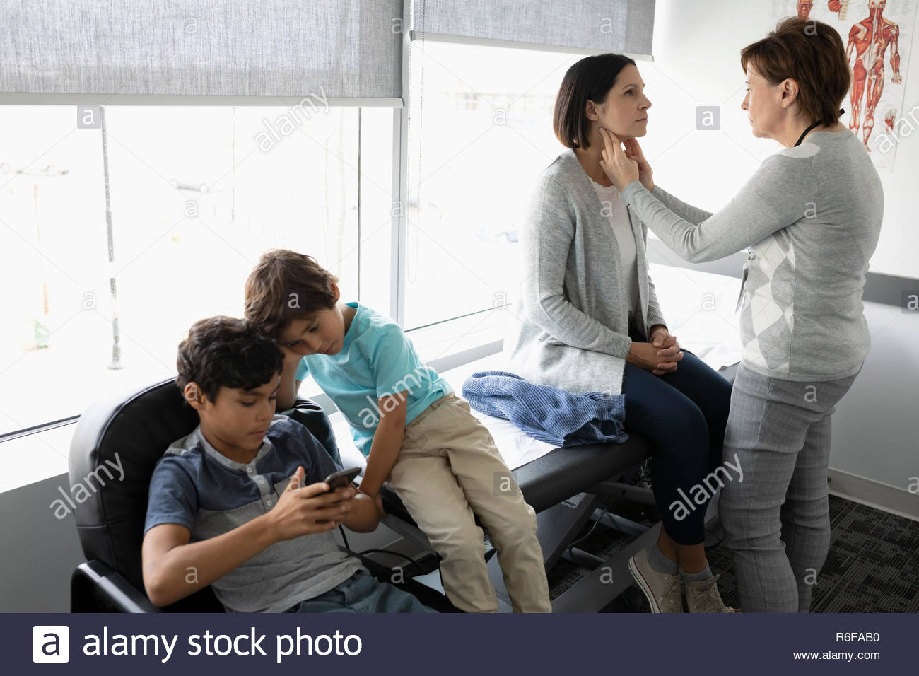 Female doctor performing checkup on mother with sons in clinic examination room Stock Photo