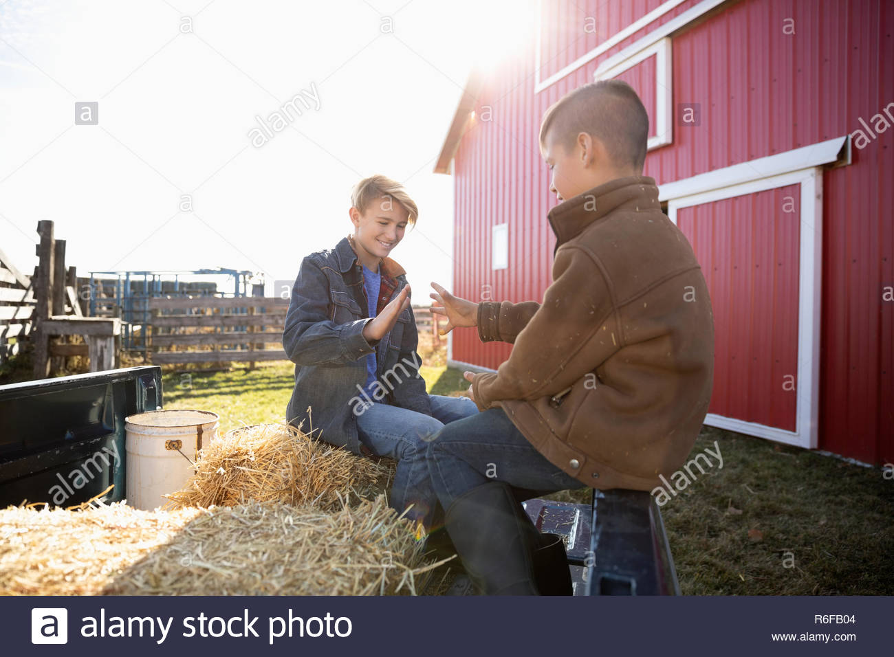 Boys playing on hay bales outside barn on sunny farm Stock Photo