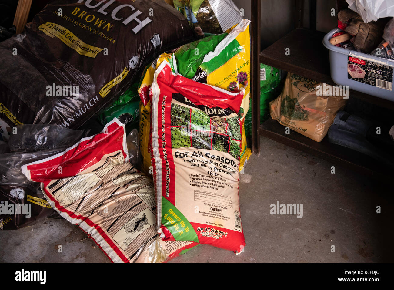 Bags of mulch, fertilizer and weed killer for lawns piled in a garage. Kansas, USA Stock Photo