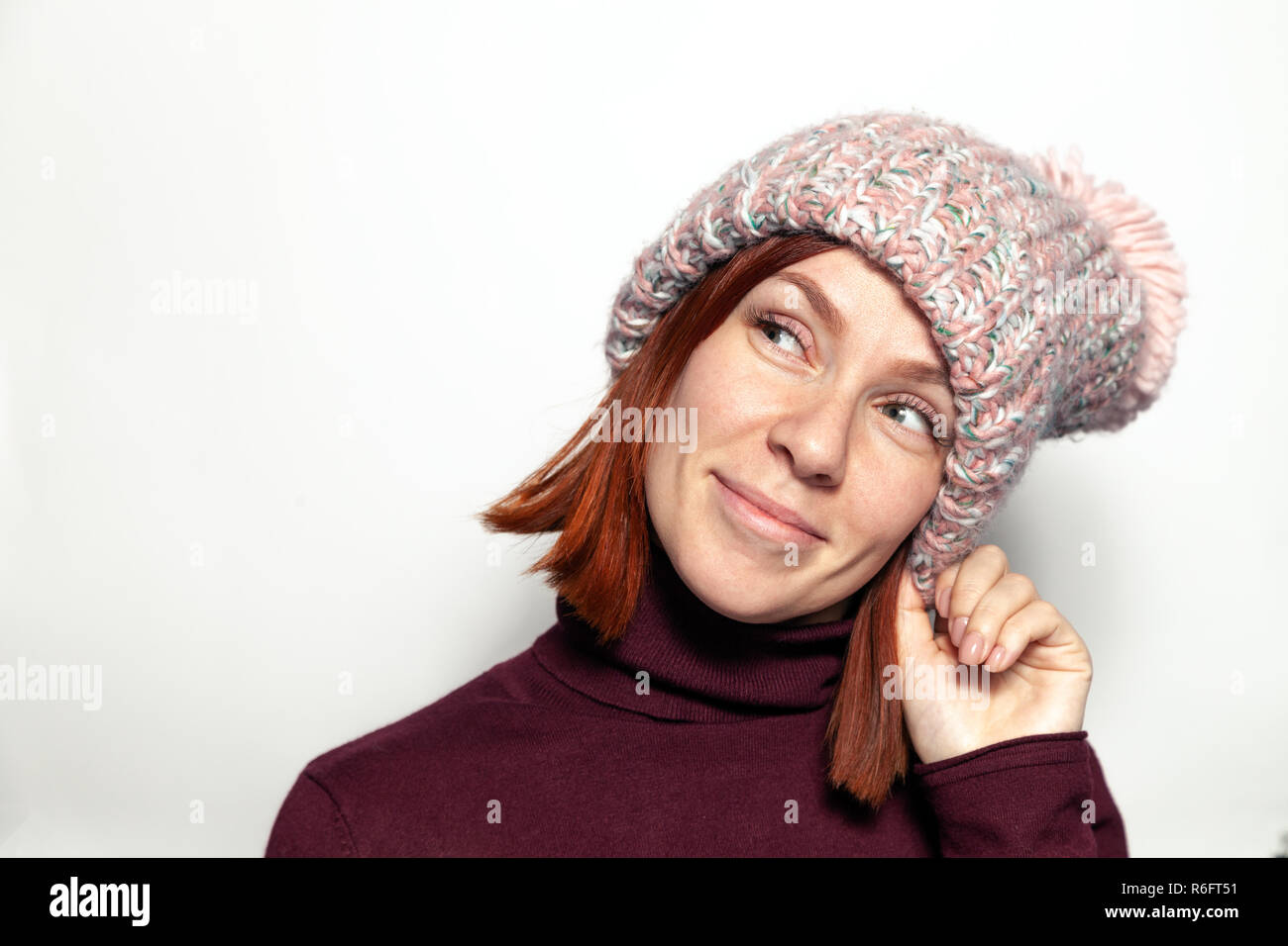 Isolated Portrait Of Beautiful Young Redhead Girl In Purple Sweater And Pink Knitted Hat With Pompon Dressed Sideways Smiling On White Background In S Isolated Portrait Of Beautiful Young Redhead Girl In Purple Sweater And Pink Knitted Hat With Pompon Dressed Sideways Smiling On White Background In S