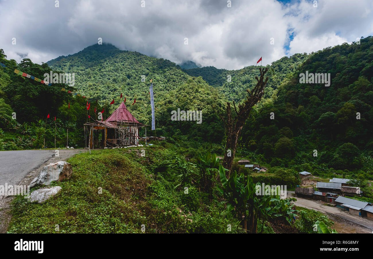 Hindu/Buddhist shrine and shanty town flanked by forested Himalayas on highway to Tawang, Arunachal Pradesh, India. Stock Photo