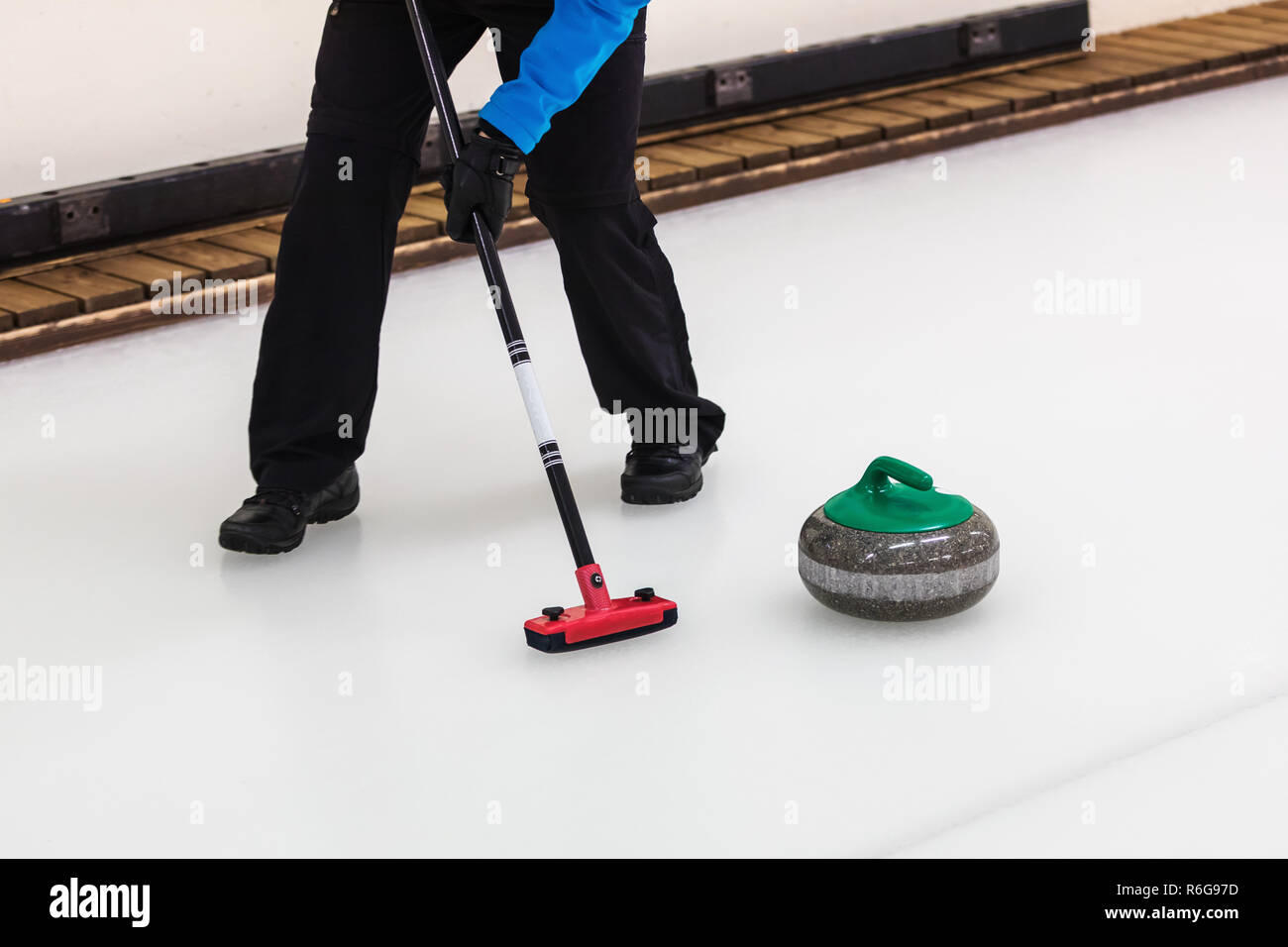 curling sport - player with broom sweeping the ice before stone ...