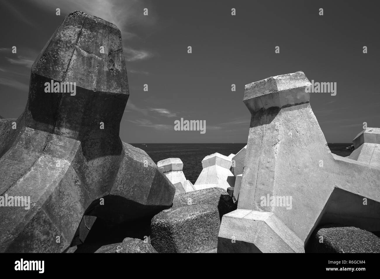 Breakwater blocks made of concrete are under dark sky. Black and white industrial background photo Stock Photo