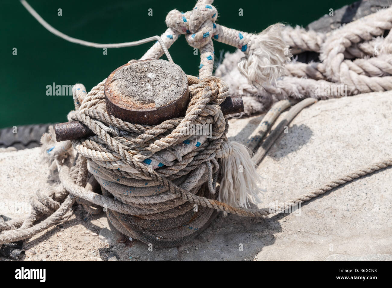 Old rusted mooring bollard with naval ropes stands on concrete pier in harbor Stock Photo