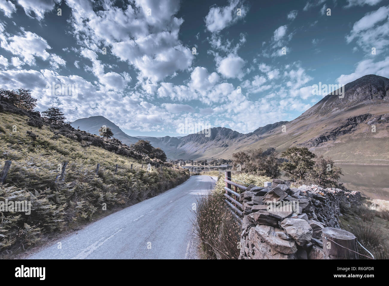 Country road with view on scenic mountain valley with lake and cloudy sky above hills of  Cumbria,UK.Nature abstract with unusual color cast.Transport Stock Photo