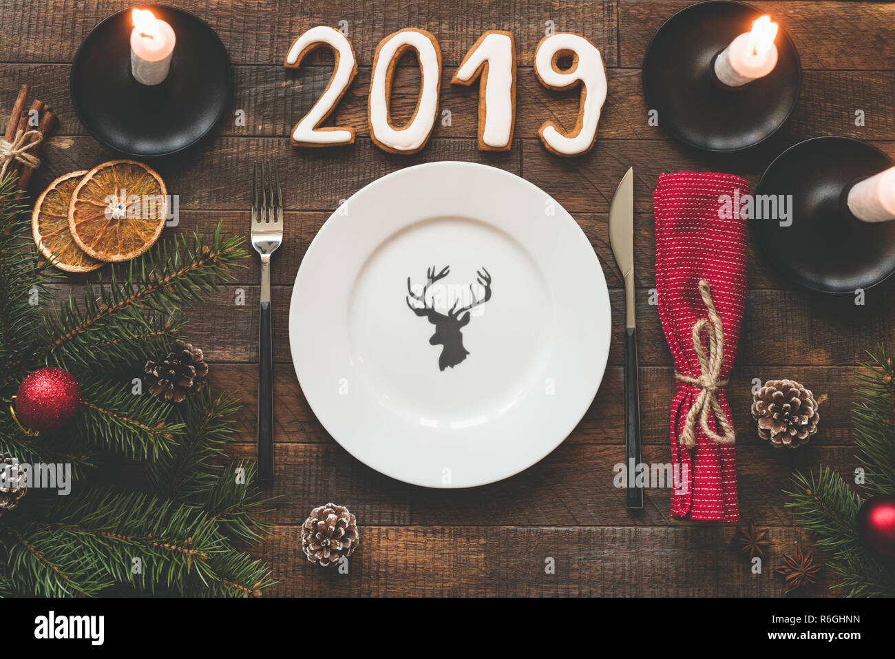 Table setting for Christmas or New Year 2019. Empty plate, silverware, red textile and candles on rustic wooden background Stock Photo