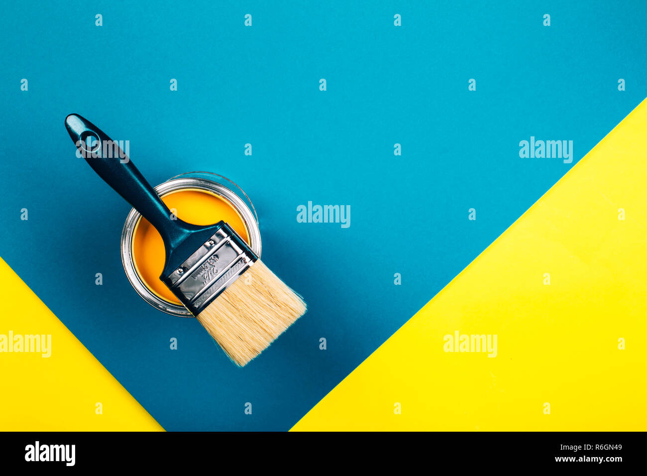 Brush on open can of yellow color paint on yellow and blue background. Flat lay style. Renovation concept. Stock Photo
