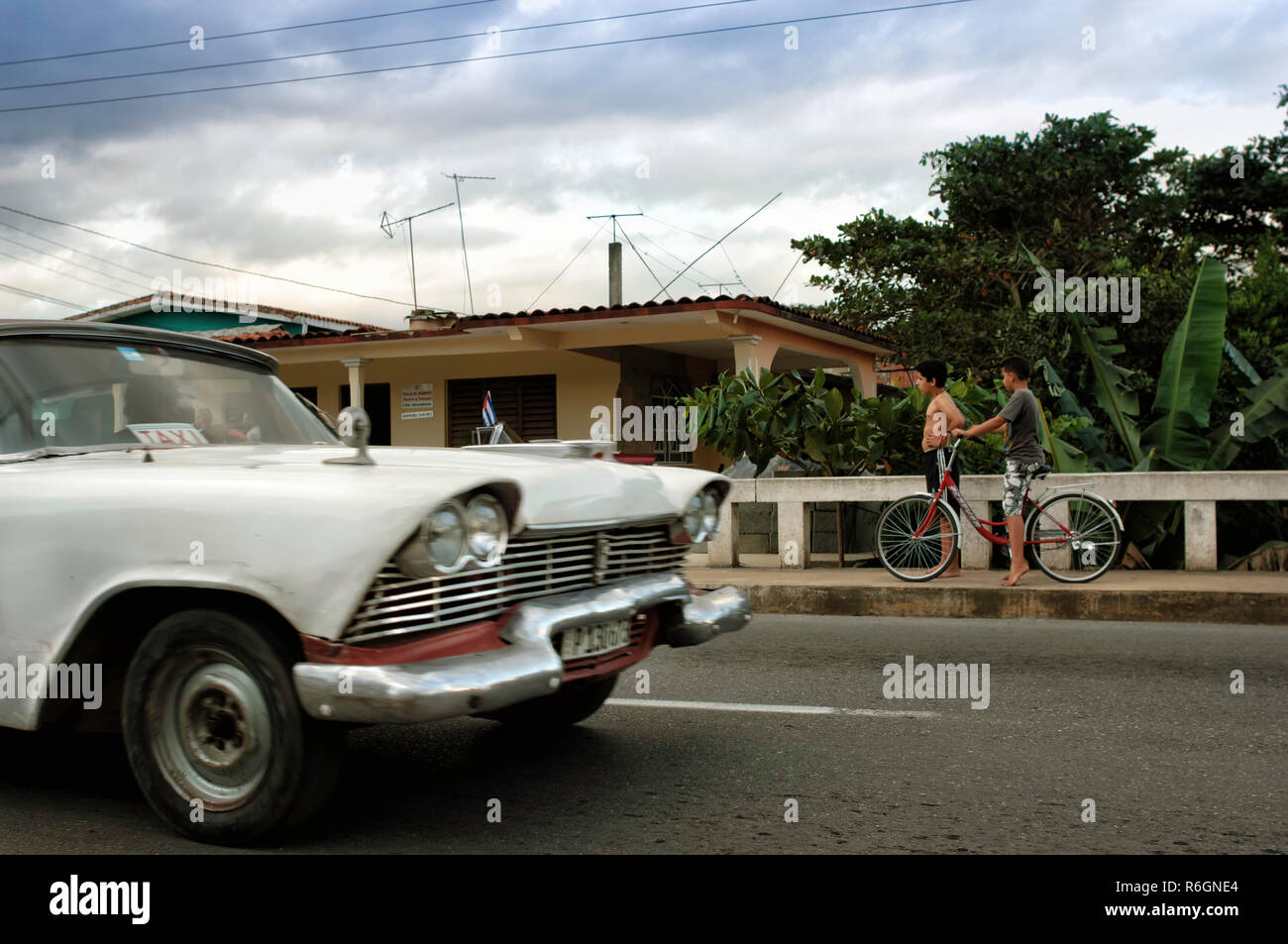 Two boys outside their house, while a classic white car drives by. Pinar del Rio, Cuba Stock Photo