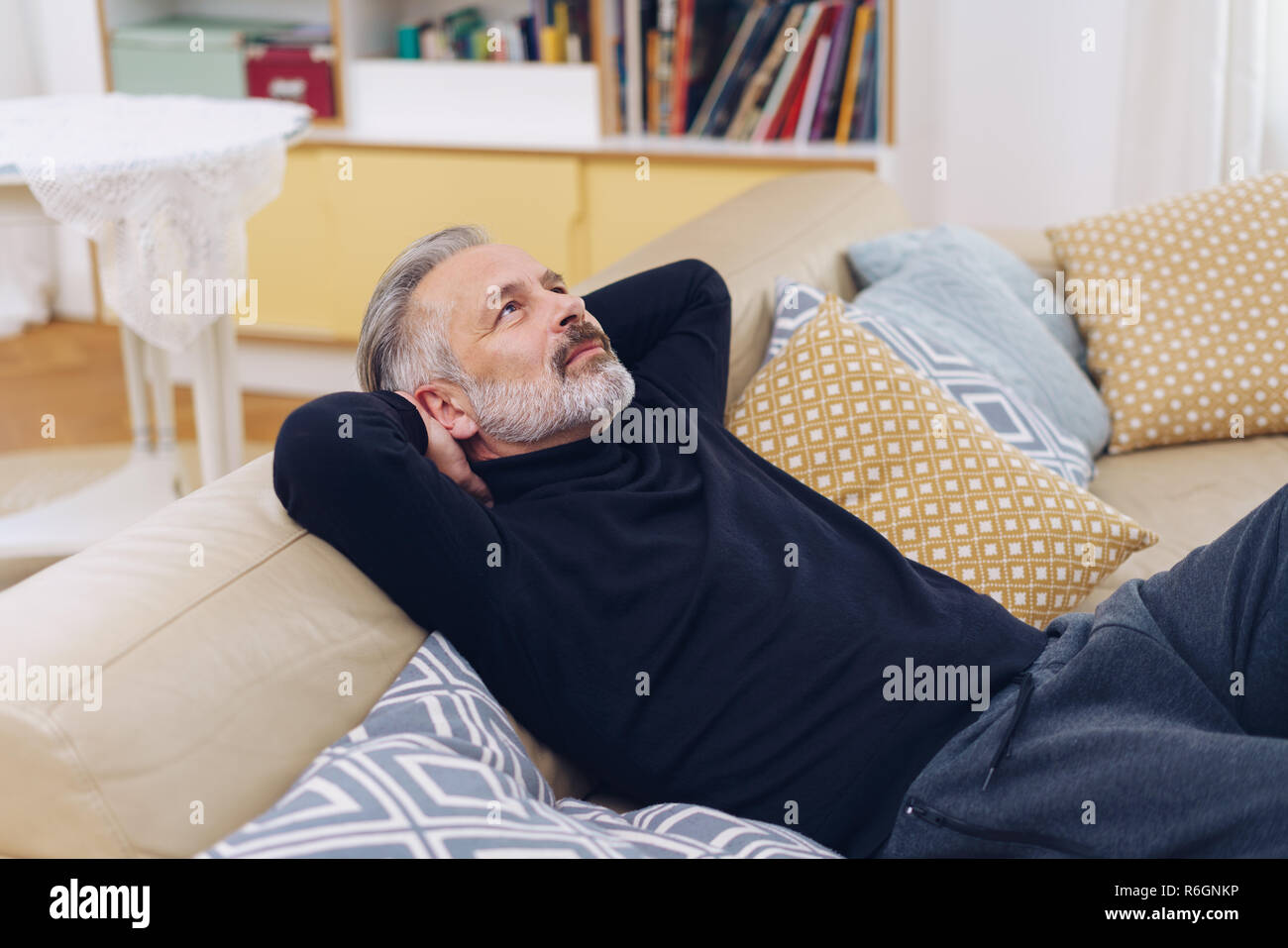 Relaxed middle-aged man looking up and daydreaming about future plans while sitting on the sofa at home Stock Photo