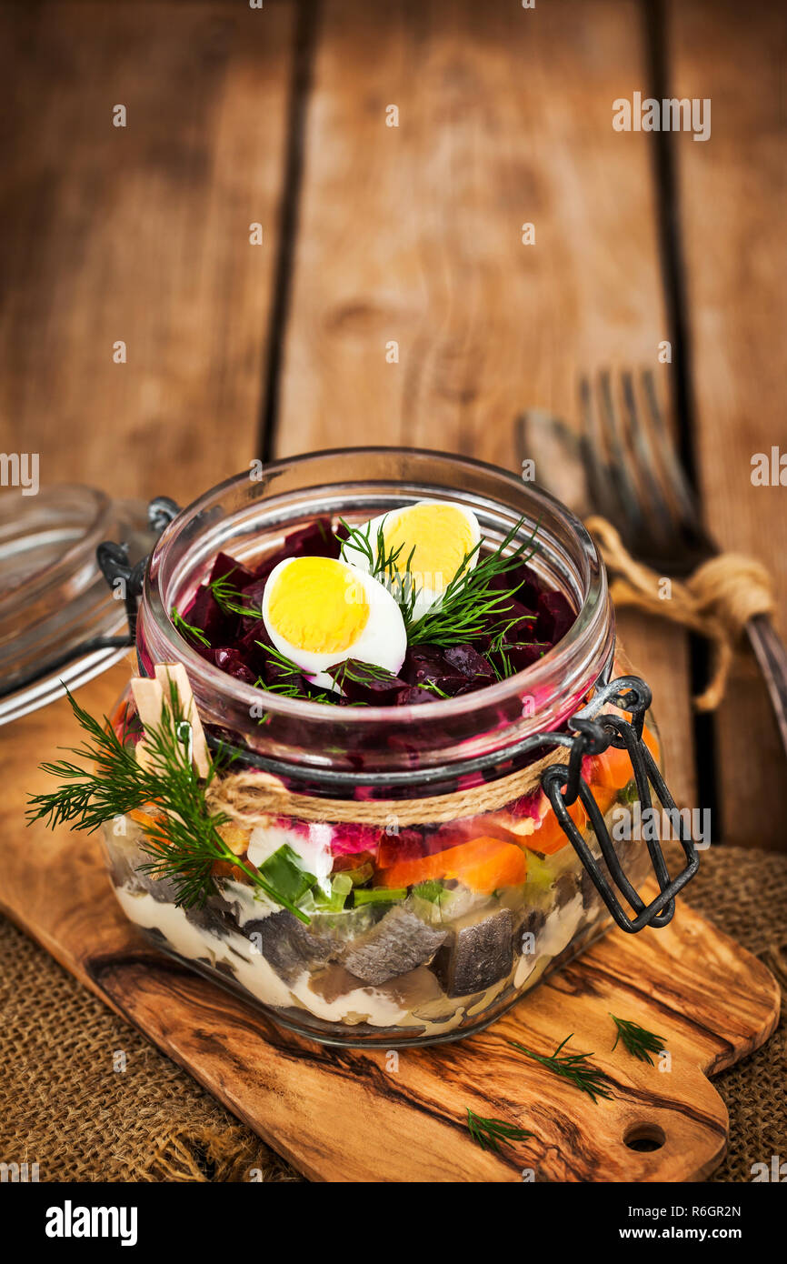 Traditional Russian layered betroot and herring salad (under a fur coat) in glass jar, rustic wooden background, selective focus Stock Photo