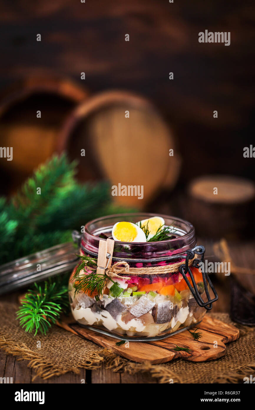 Traditional Russian layered betroot and herring salad (under a fur coat) in glass jar, rustic wooden background, selective focus Stock Photo