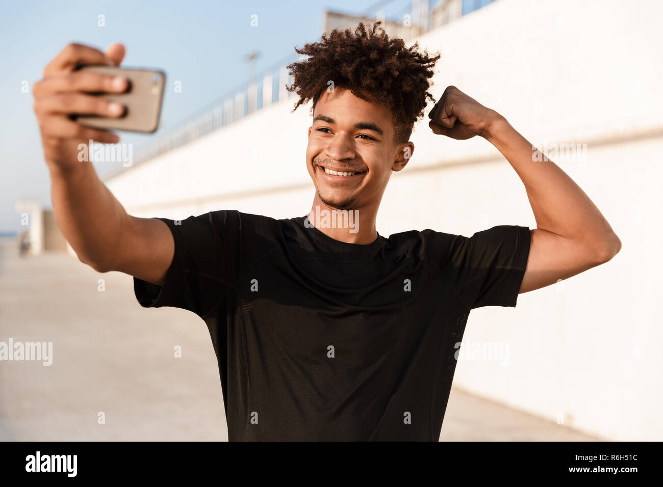 Smiling young african teenager sportsman standing at the beach, taking