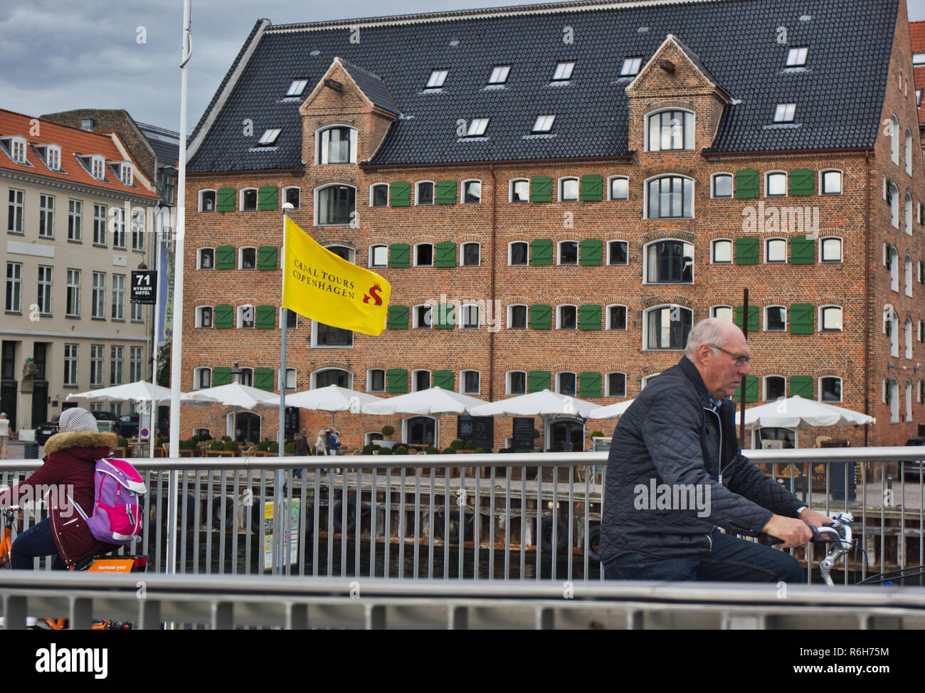Cyclists on Inderhavnsbroen (Inner Harbour Bridge) with a preserved Nyhavn warehouse in the background, Nyhavn, Copenhagen, Denmark, Scandinavia Stock Photo