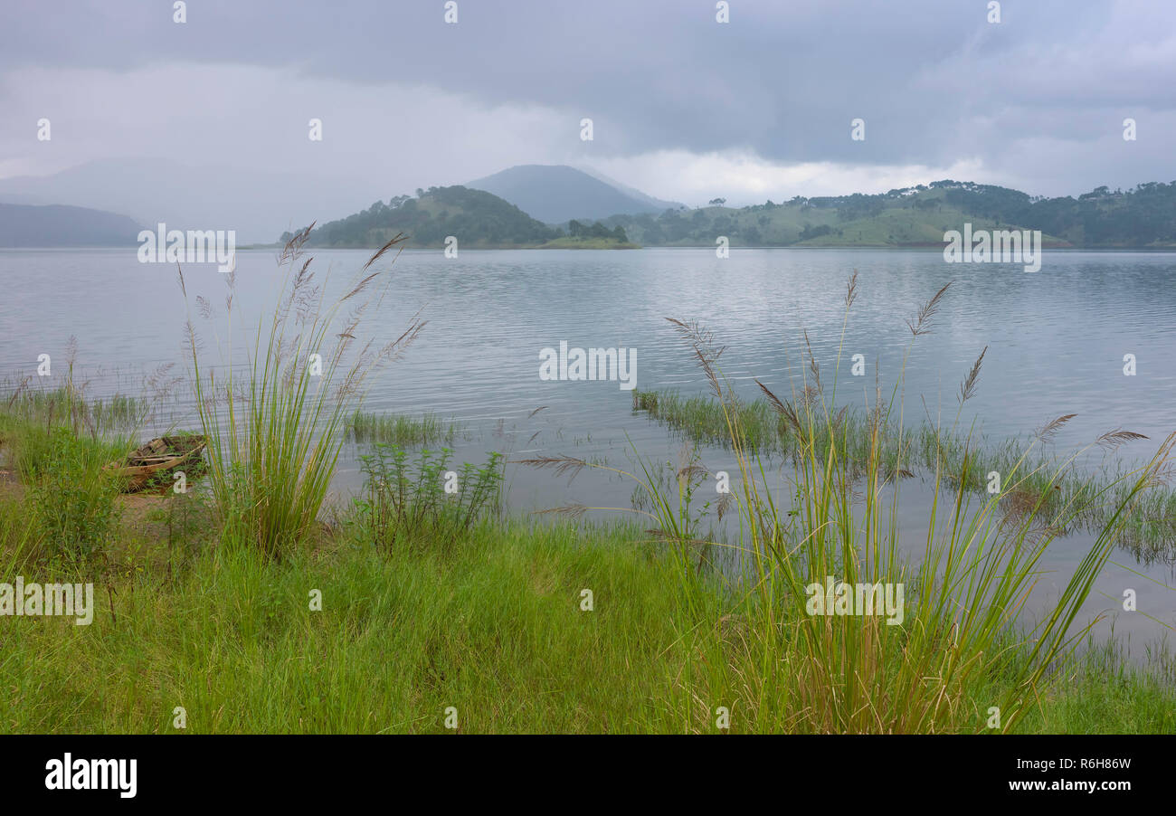Umiam Lake and moored wooden boat flanked by Khasi Hill and tall grasses on a monsoon morning, Shillong, Meghalaya, India Stock Photo