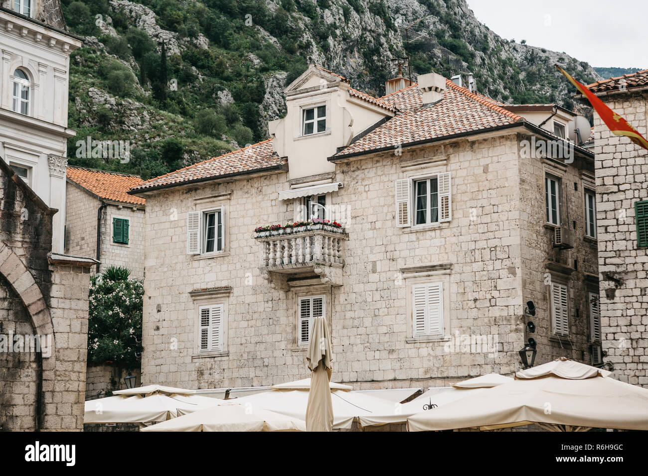The facade of an ordinary old building with windows and a balcony in Montenegro. Traditional housing. In the background is a mountain. On the building is the flag of Montenegro. Stock Photo