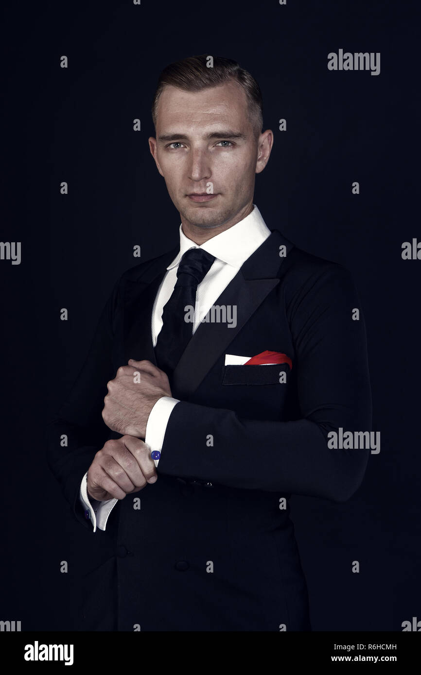 Man in a black tuxedo suit and white shirt and black tie on a black ...