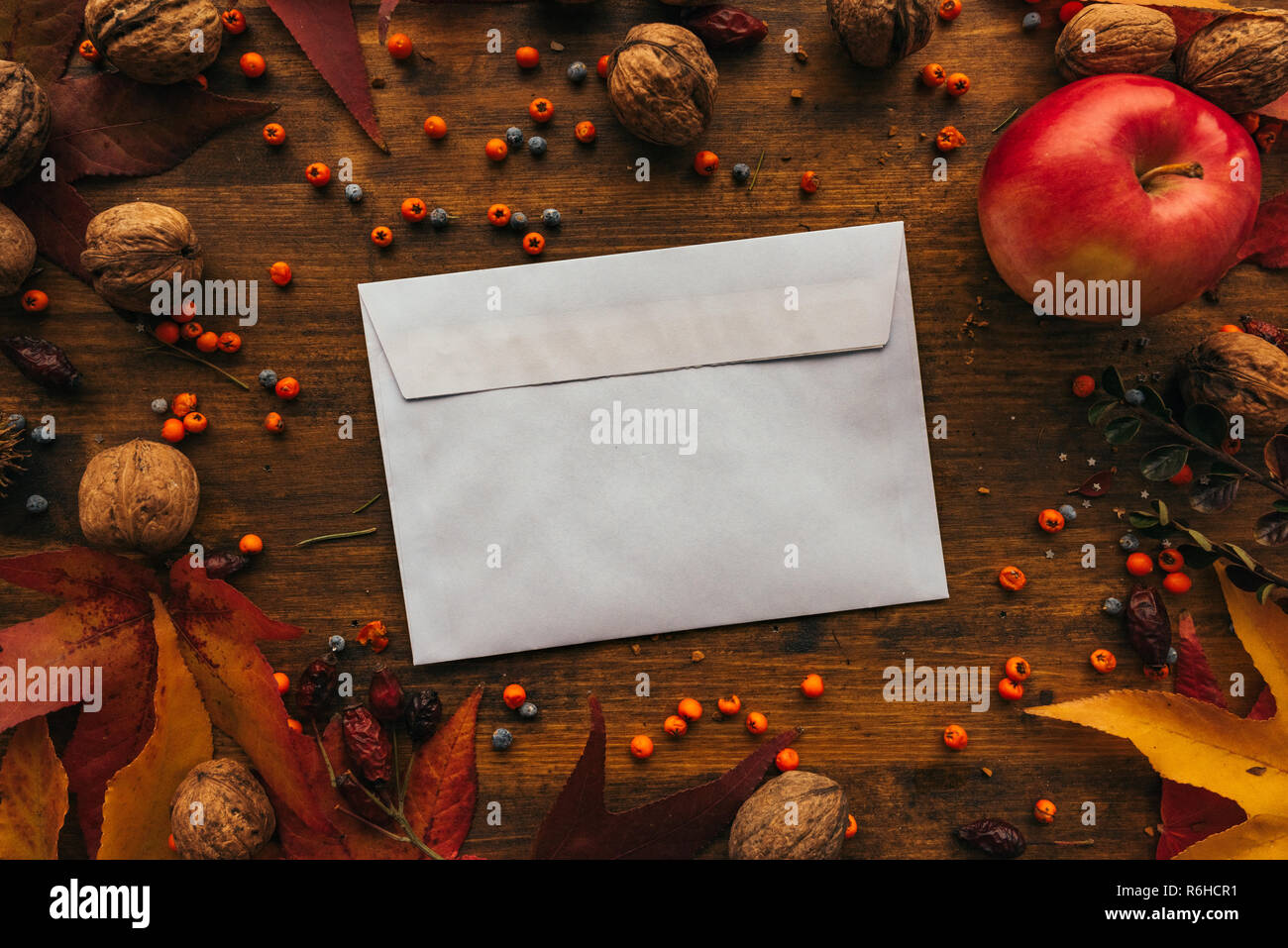 Autumn mail envelope flat lay mock up on wooden table decorated with dry maple leaves and seasonal fruit Stock Photo
