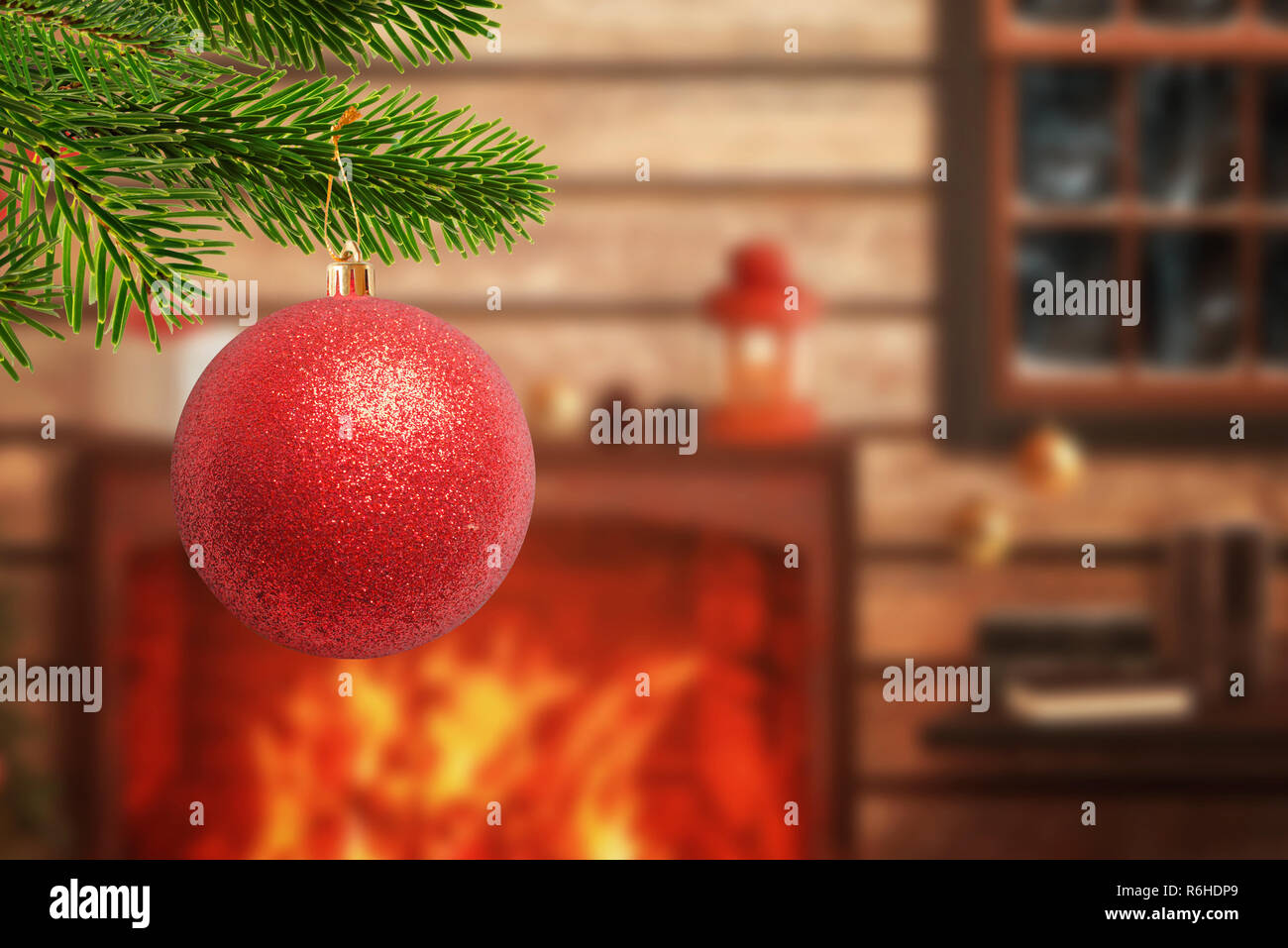 Christmas tree with decorative red ball in the foreground. Fireplace with gifts and Christmas decorations in background. Warm home atmosphere during t Stock Photo