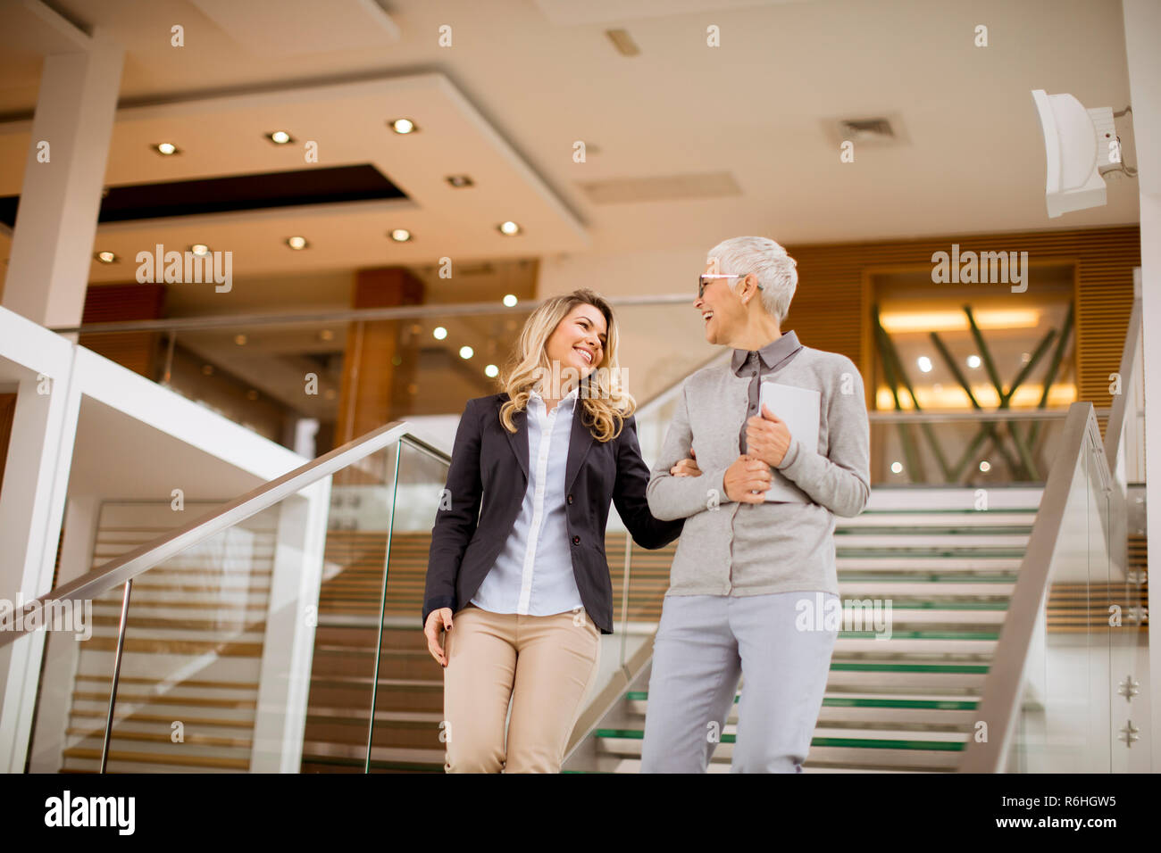 Cheerful senior and young businesswomen getting down the stairs in modern office Stock Photo