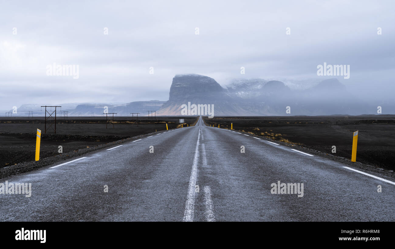 A road leading through black sanded landscape towards misty mountains in Iceland Stock Photo