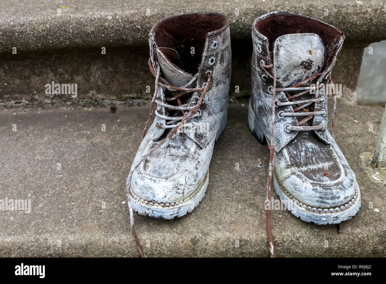 Old brown work boots. Boots smeared with white paint. Dirty boots on the stairs. Dirty old workboots on stairs. Stock Photo