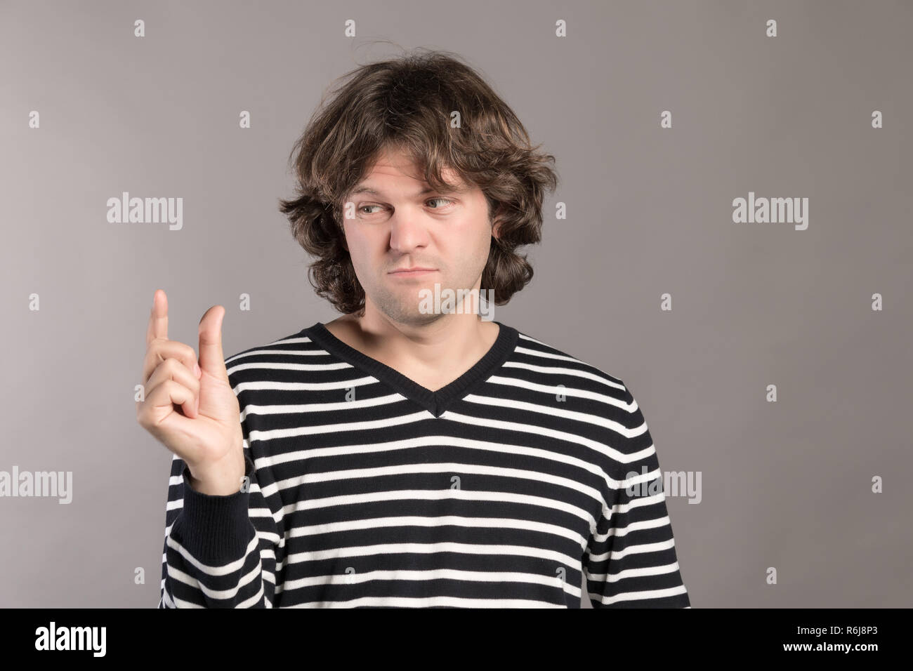 Handsome young man over grey grunge wall smiling and confident gesturing with hand doing size sign with fingers while looking and the camera. Measure concept. Stock Photo