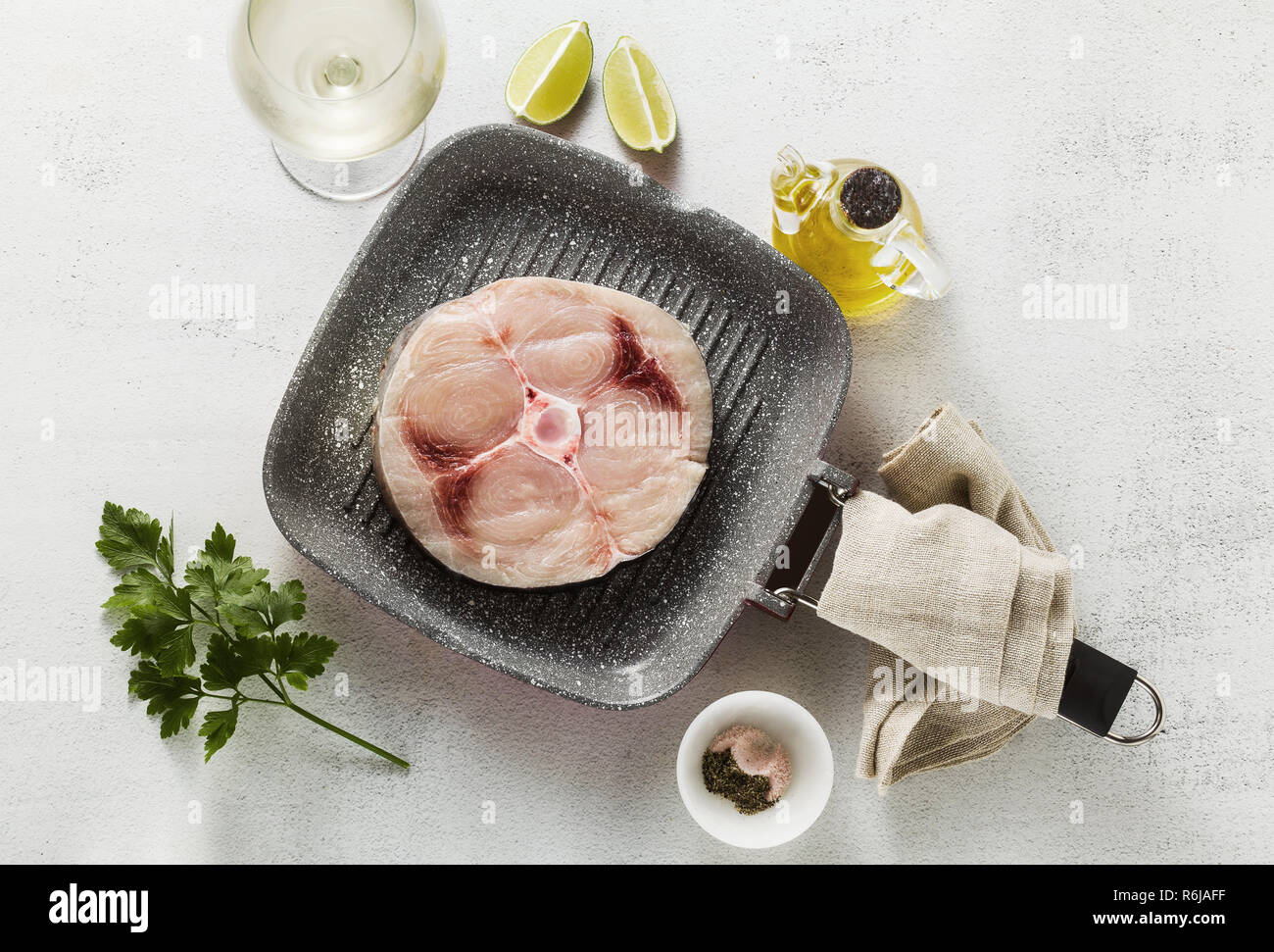 raw swordfish steak on the grill pan with olive oil and spices, white wine glass Stock Photo
