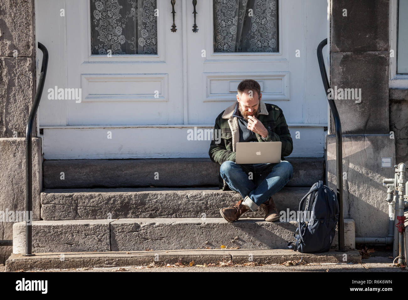MONTREAL, CANADA - NOVEMBER 4, 2018: Young Caucasian Male, digital nomad, sitting and using his laptop, Apple Macbook, to get wifi internet connection Stock Photo